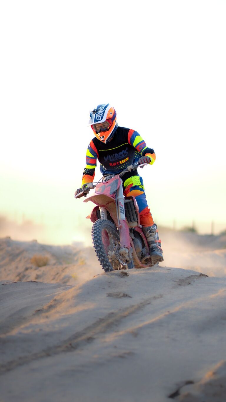 Motocross rider in bright gear racing over sand dunes